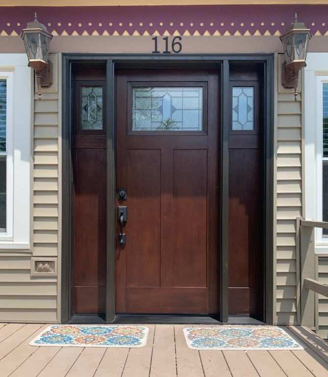 Brown wooden front door with sidelights, decorative lights, and house number 116.