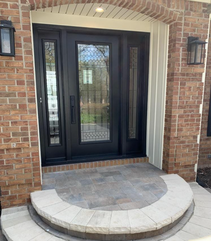 Black front door with sidelights, brick exterior, and a small curved stone entryway.