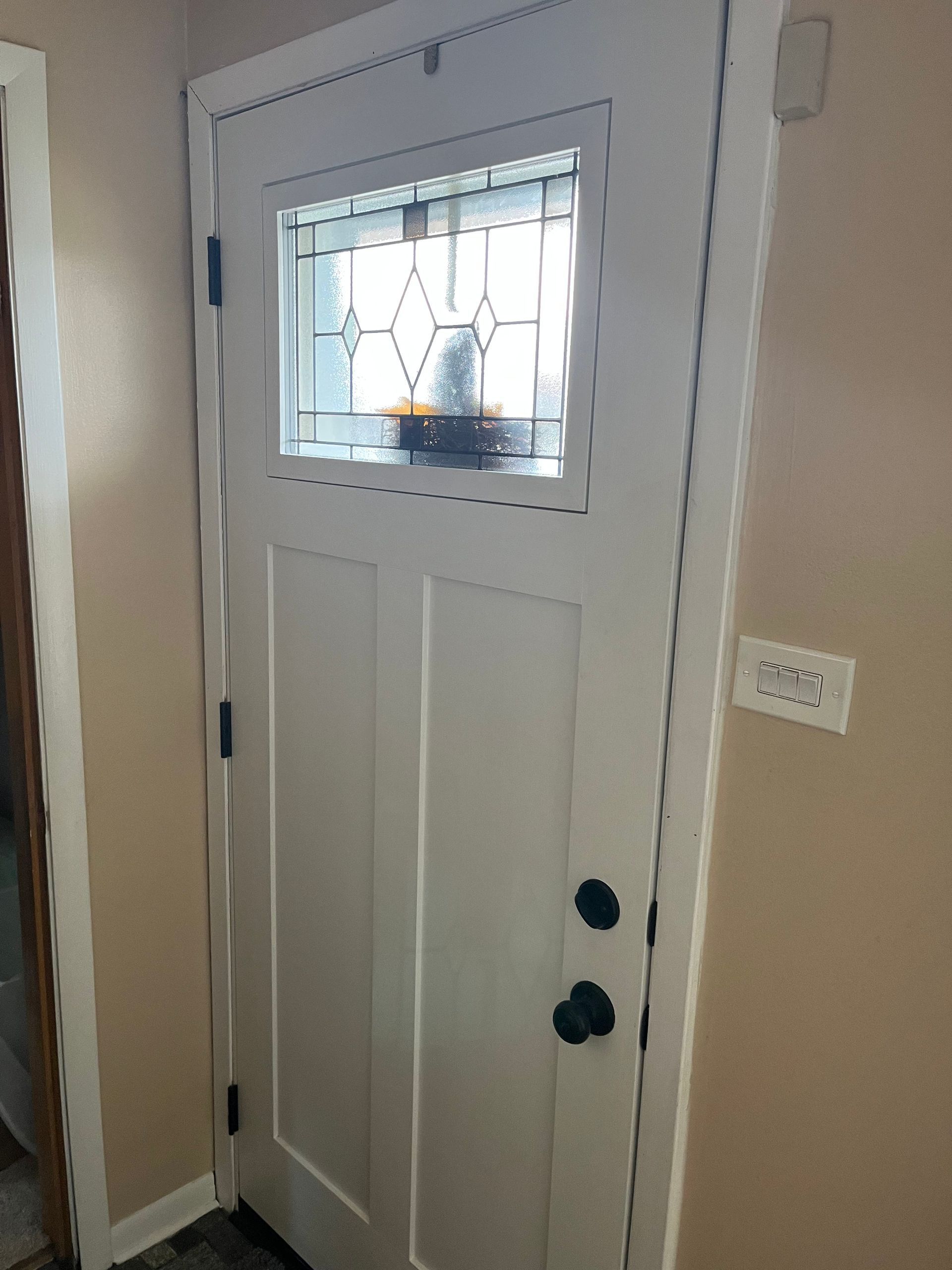 White front door with stained glass window, black hardware, beige walls.