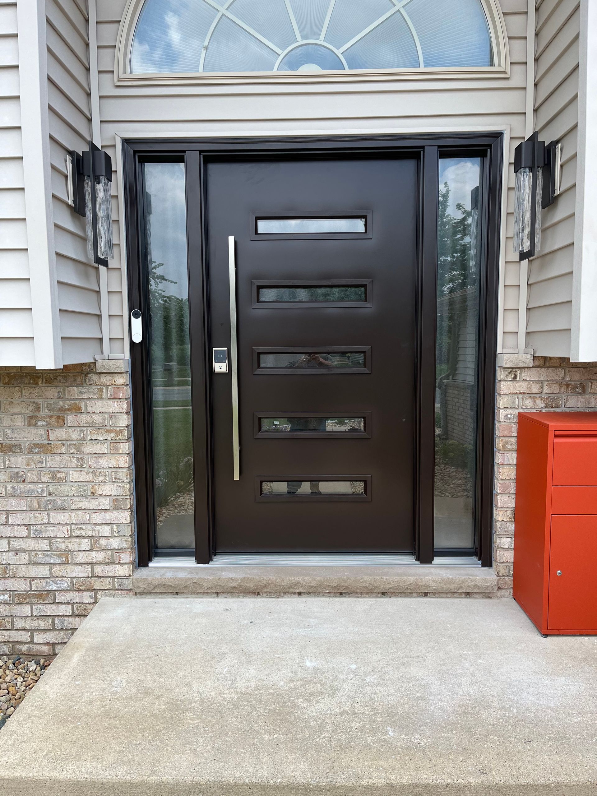 Modern brown front door with sidelights, handle, and horizontal glass panels. Red mailbox on the right.