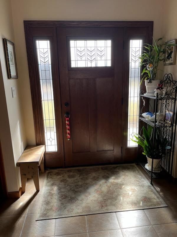 Wooden front door with sidelights, rug, bench, and plants.