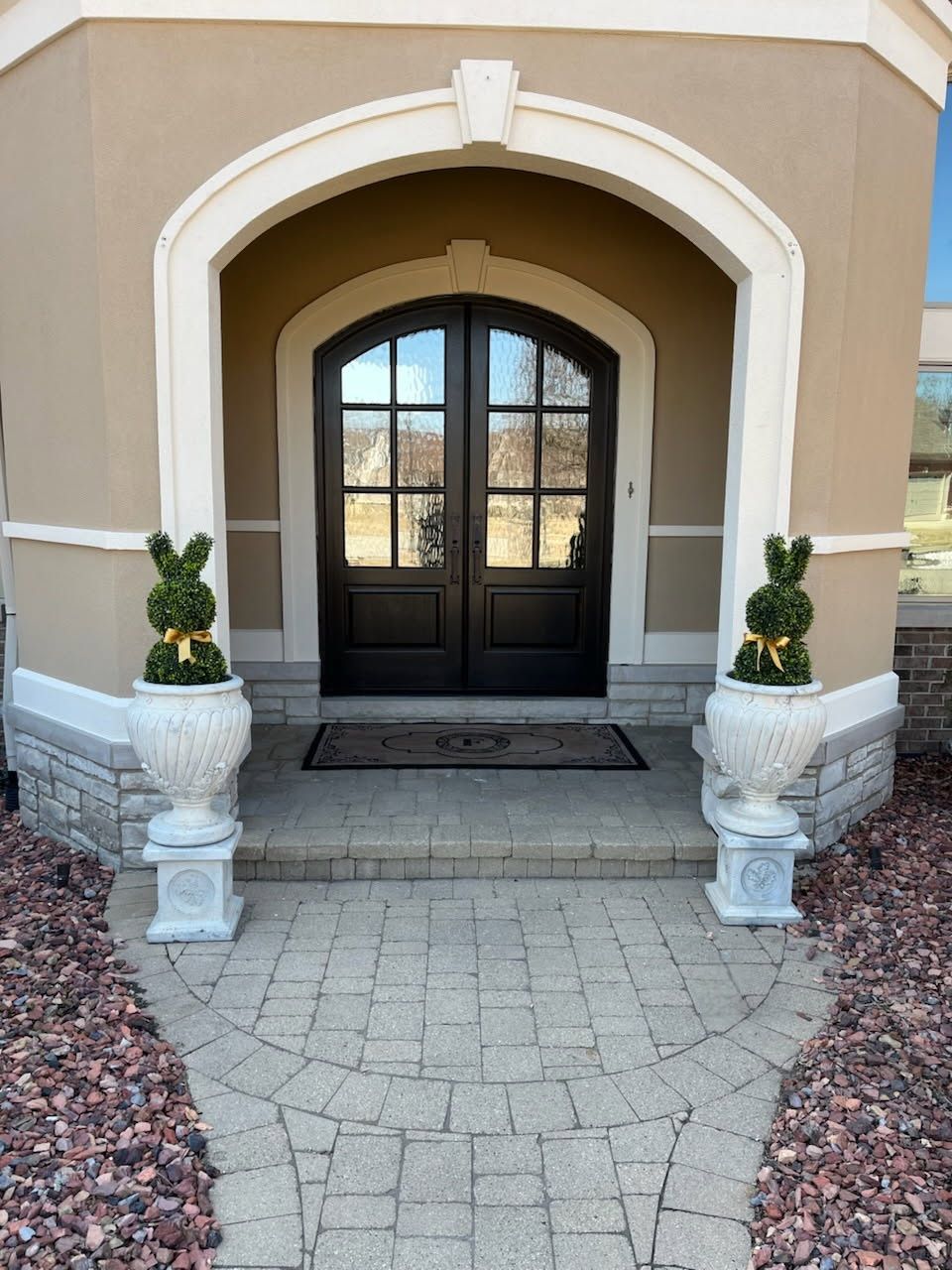 Front entrance with arched doorway, double doors, and bunny-shaped topiary plants in white urns.