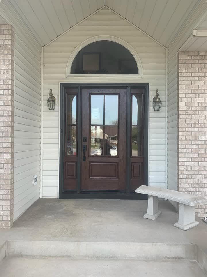 Brown front door with sidelights and arched window above, set in a covered entryway. Concrete bench on the porch.