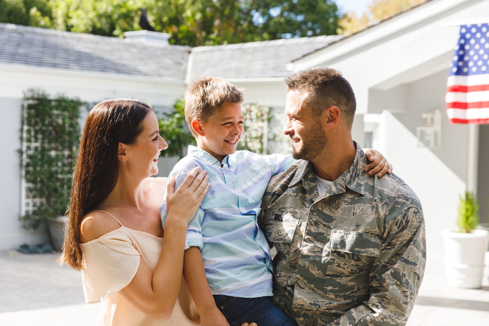 A man in a military uniform is holding a boy and a woman.