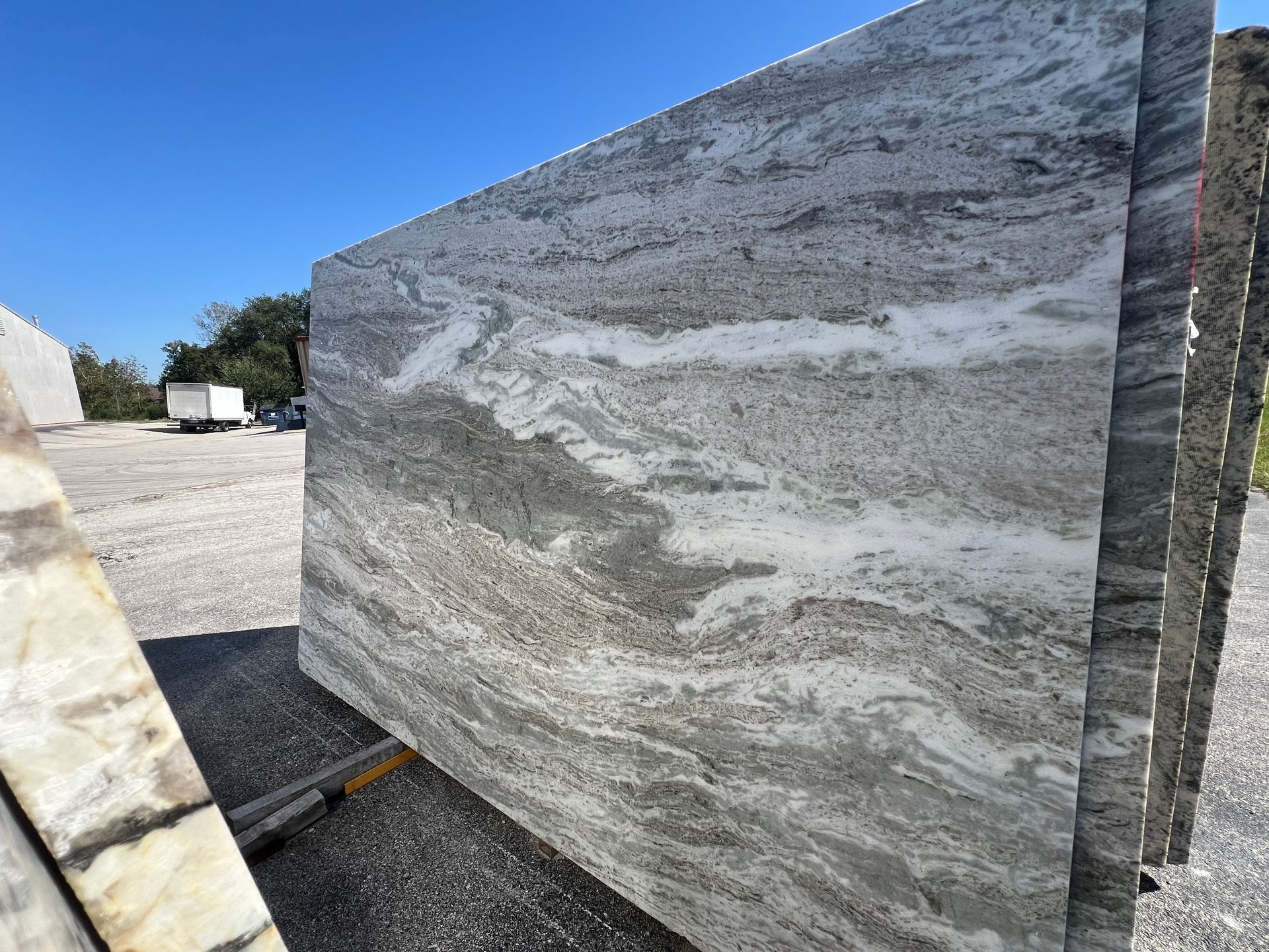 Large gray and white marble slab outdoors in a stone yard under bright sunlight