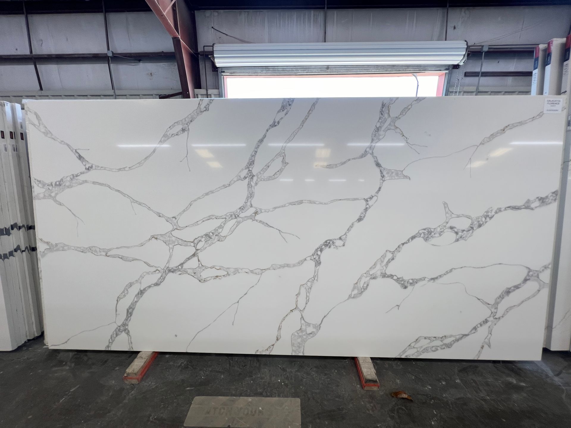 Large white marble-look slab with gray veining displayed in a warehouse or stone showroom.