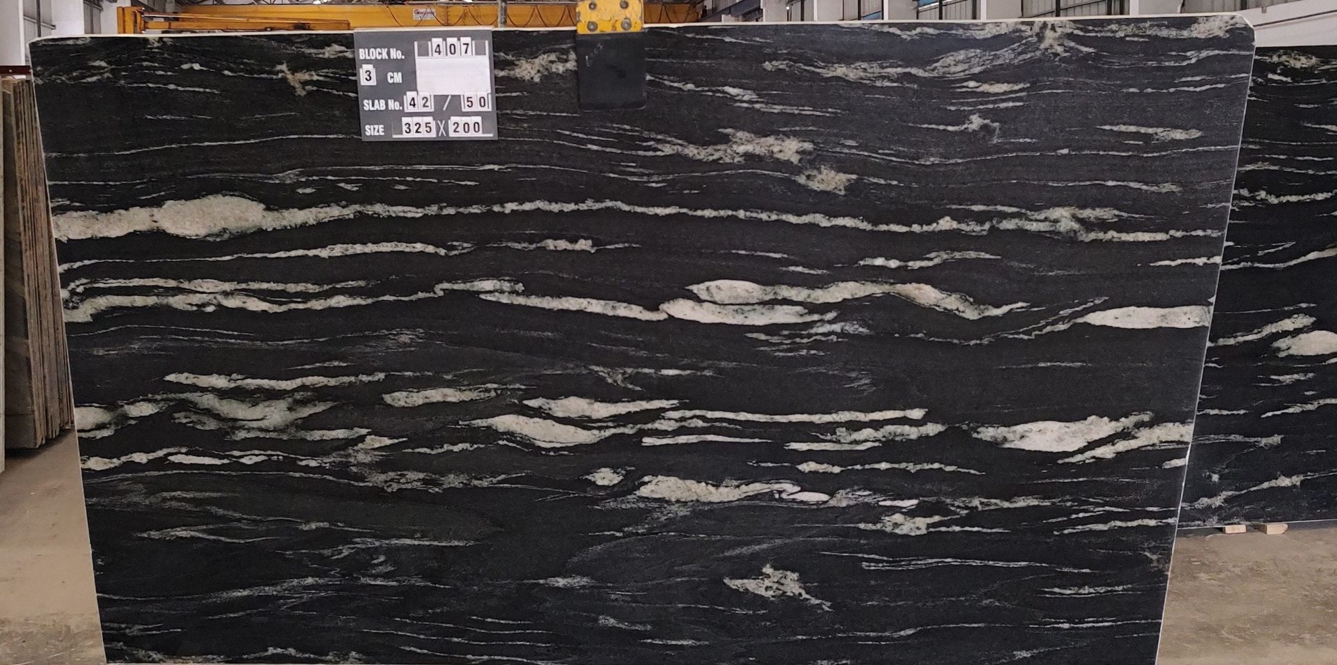Black marble slab with white veining, standing upright in a warehouse or showroom.