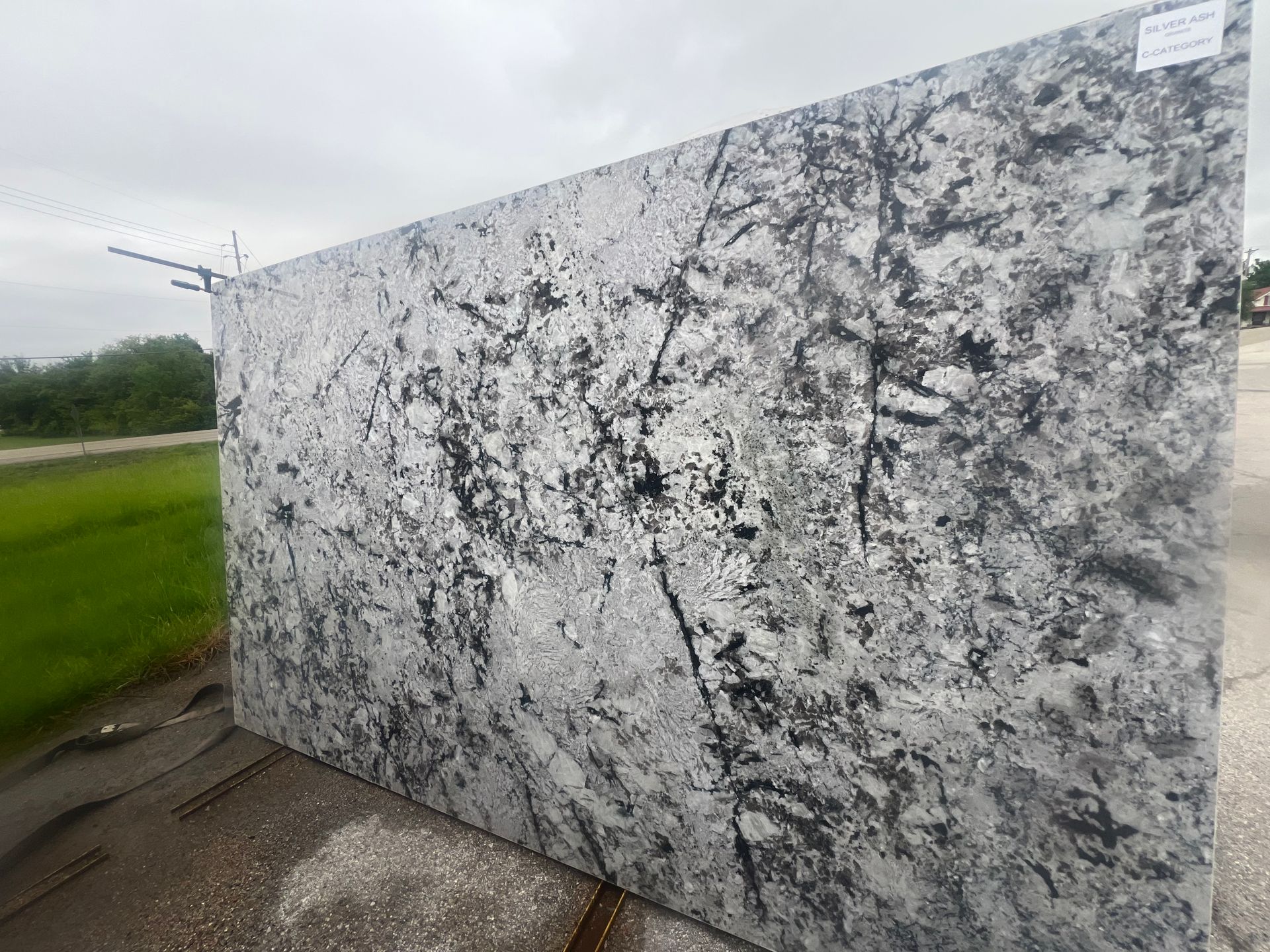 Large gray-and-black speckled marble slab standing outdoors beside a grassy road