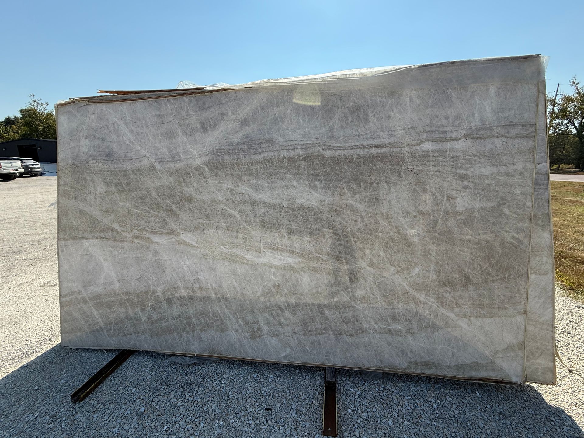 Large gray concrete slab outdoors on a gravel lot, with a blue sky and trees in the background