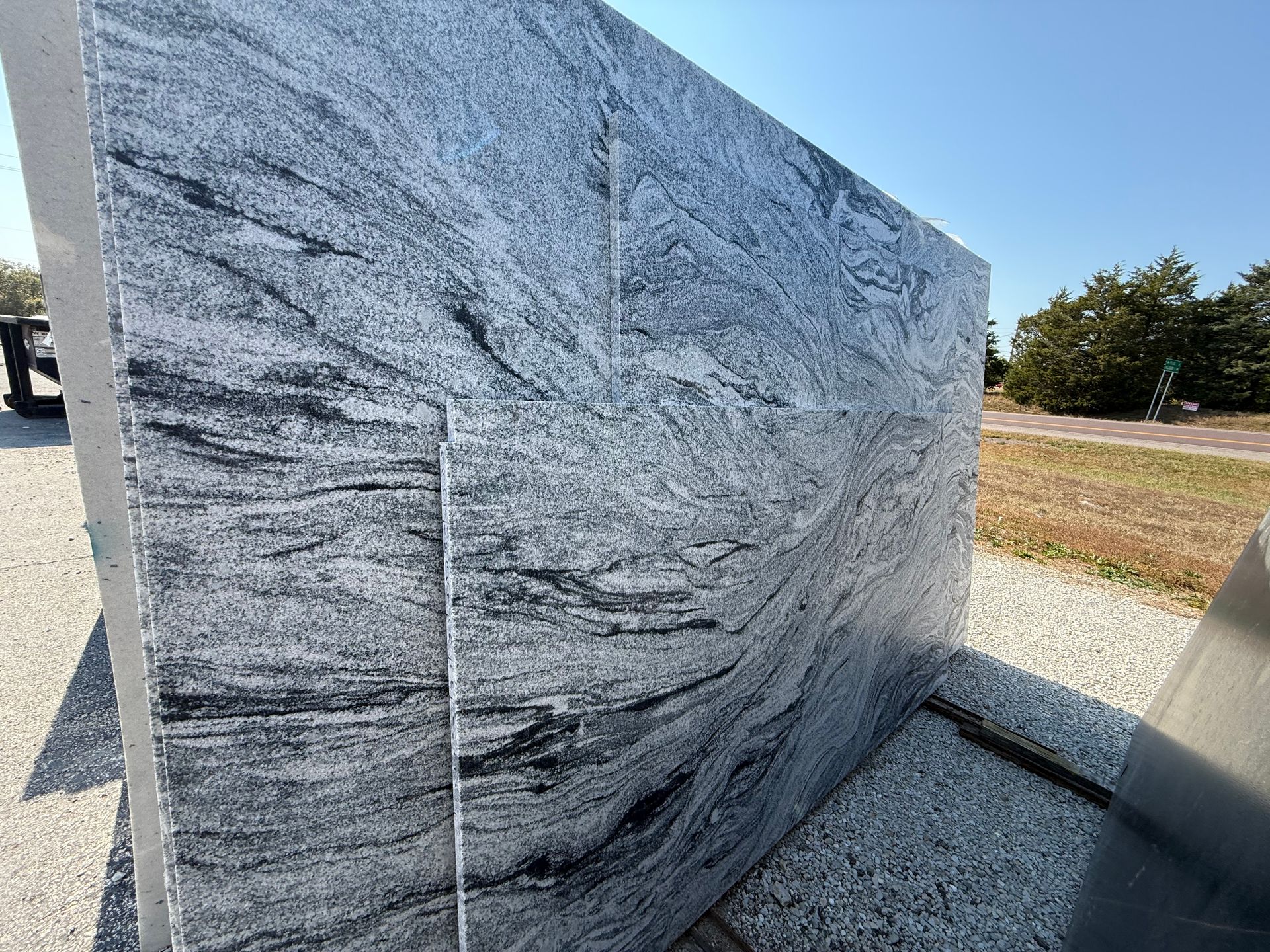 Large gray granite monument with swirling patterns outdoors in a sunny park