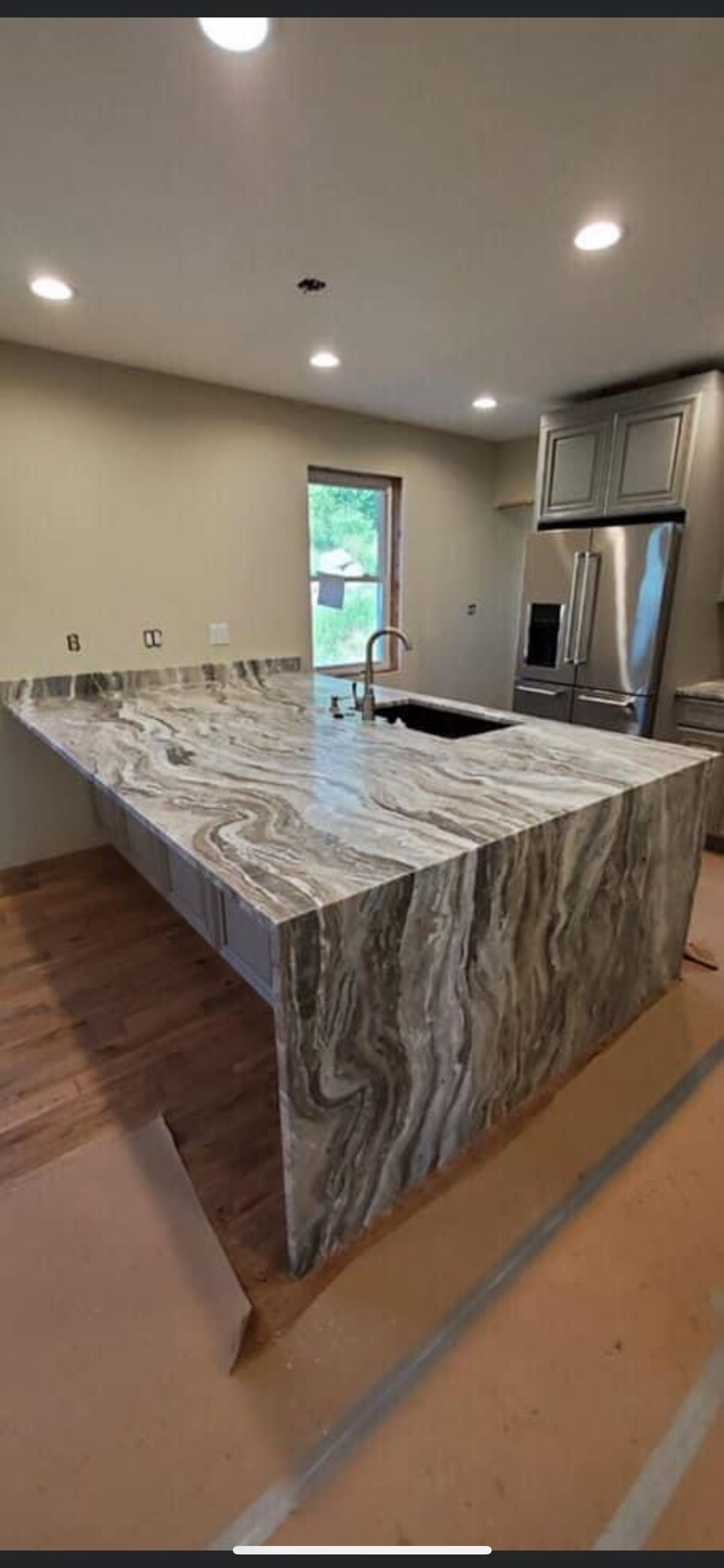 Modern kitchen with a large marble island, stainless appliances, and recessed ceiling lights.
