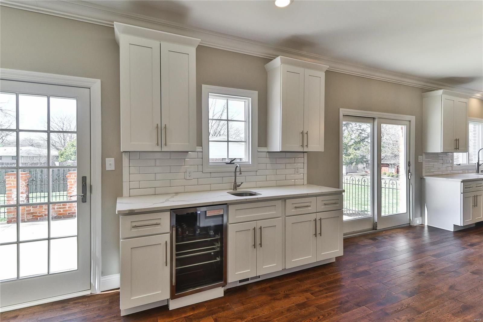 Bright kitchen with white cabinets, gray backsplash, dark wood floors, and French doors to a patio.