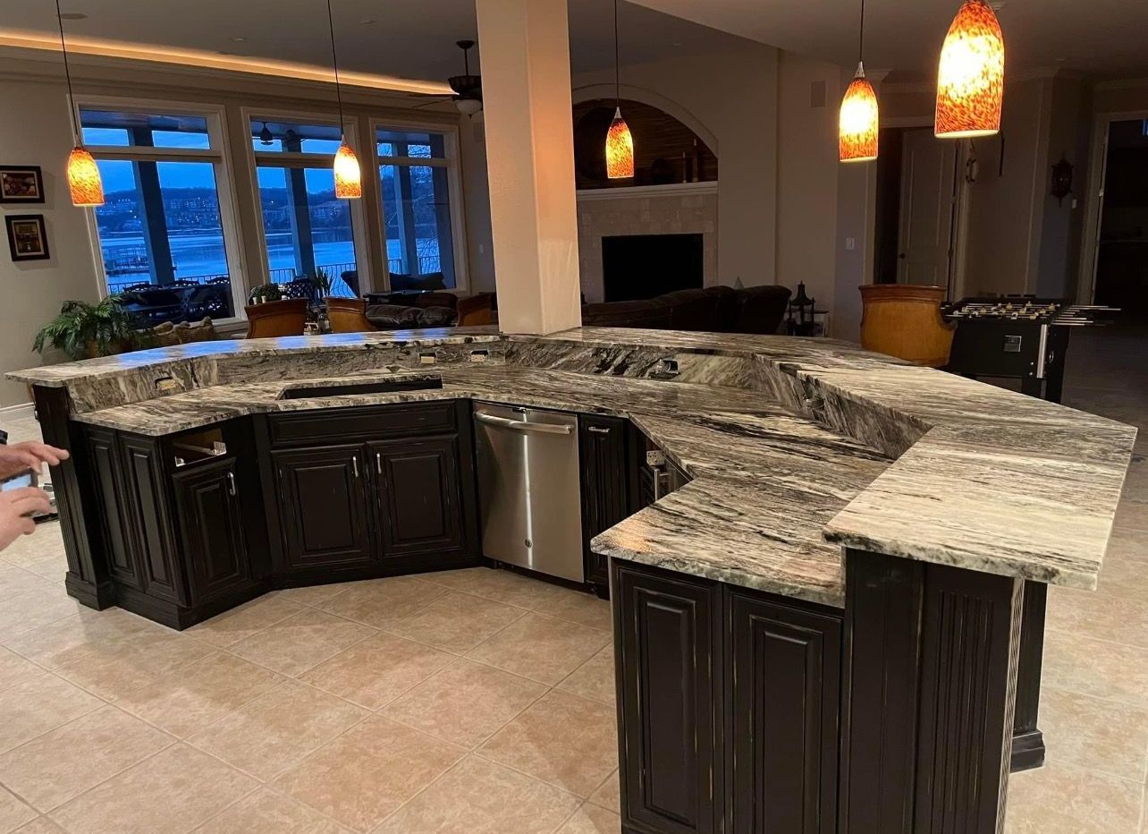 Large kitchen with dark cabinets and a granite island counter under warm pendant lights.