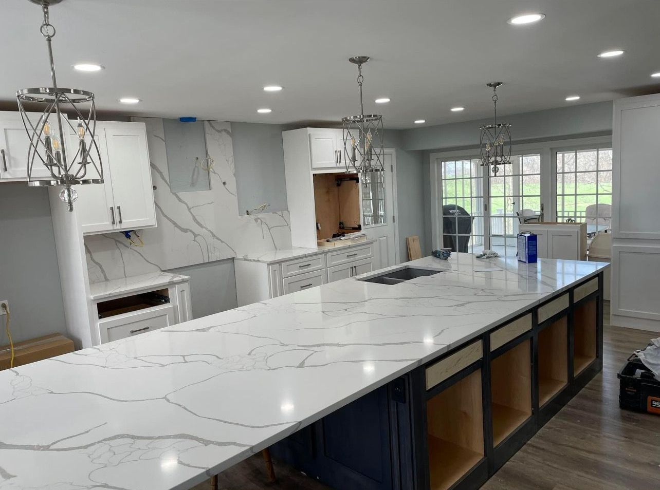Bright modern kitchen with white marble island, black cabinets, and recessed ceiling lights