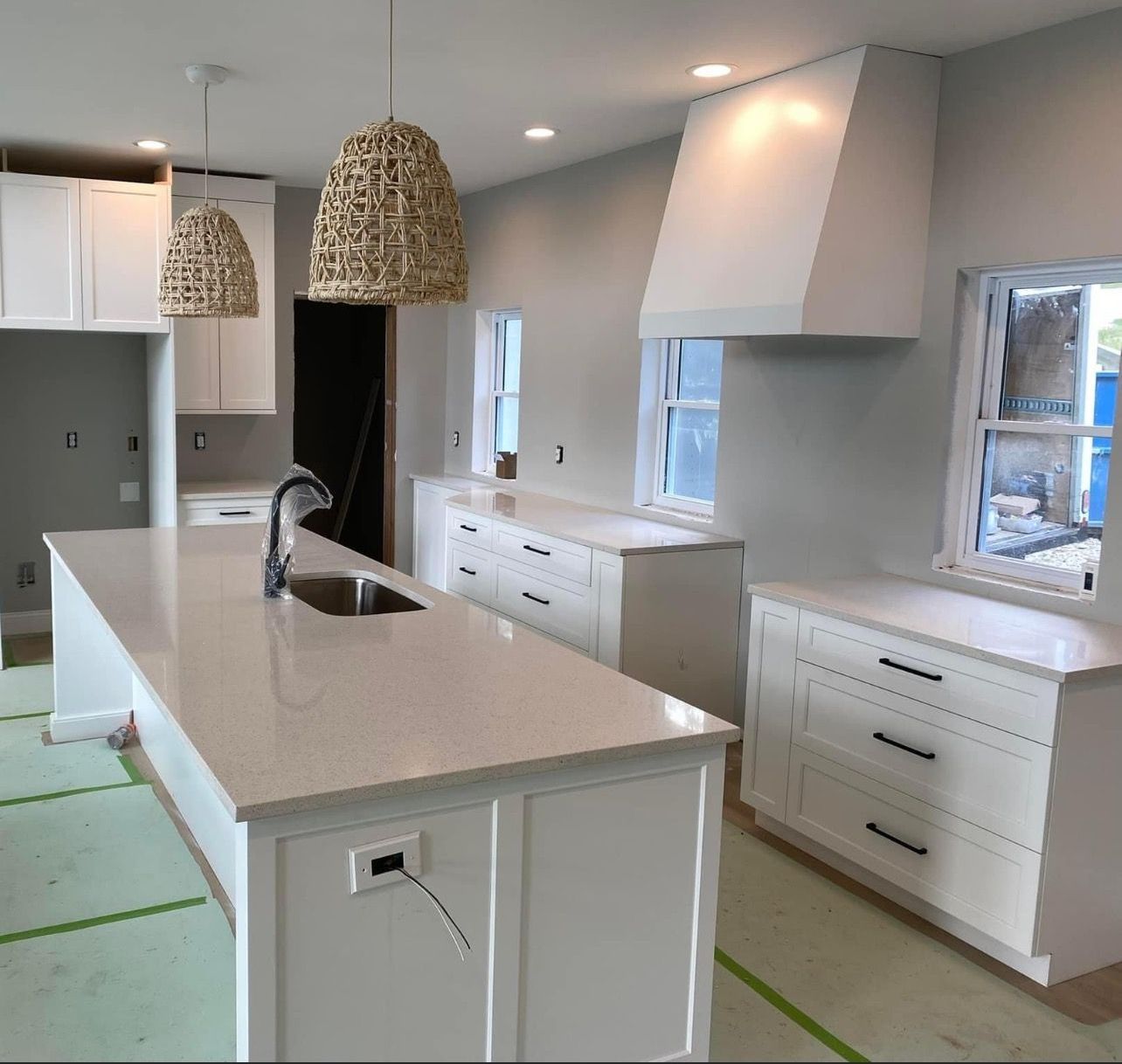 Bright modern kitchen with white cabinets, island, pendant lights, and unfinished flooring/paint masking tape.