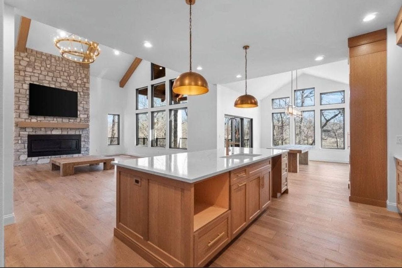 Modern open-concept kitchen with wood island, white counters, pendant lights, and stone fireplace in bright living area