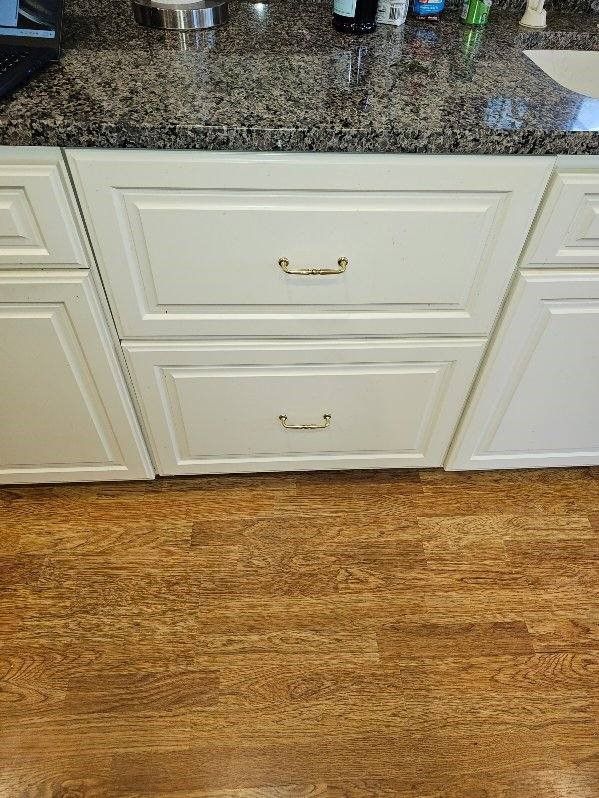 Kitchen cabinets with brass handles beneath a speckled granite countertop and wood floor