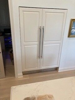 White double-door refrigerator built into wall, stainless steel handles, in kitchen.