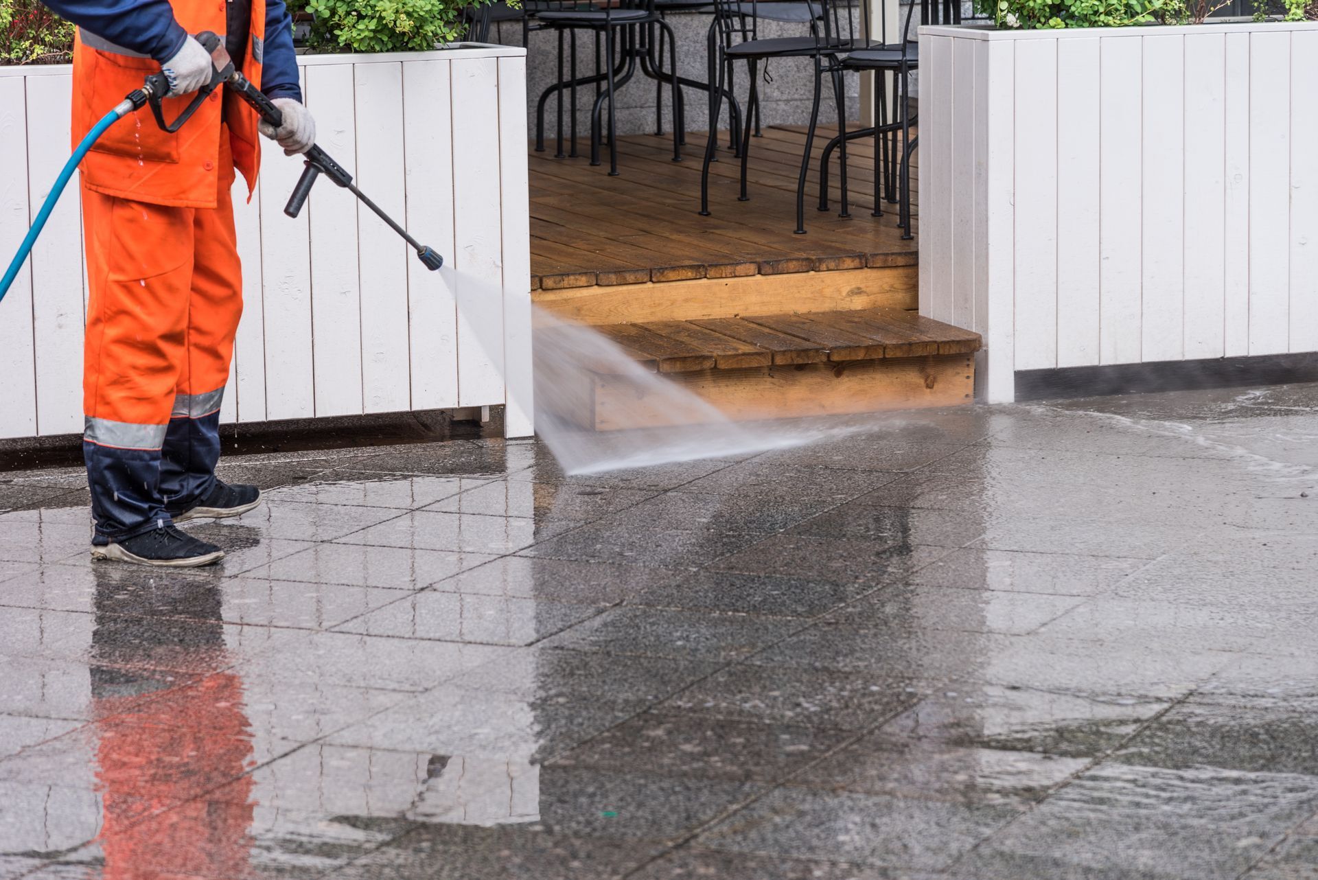 Worker cleaning sidewalk, showcasing commercial pressure washing in front of a street café.
