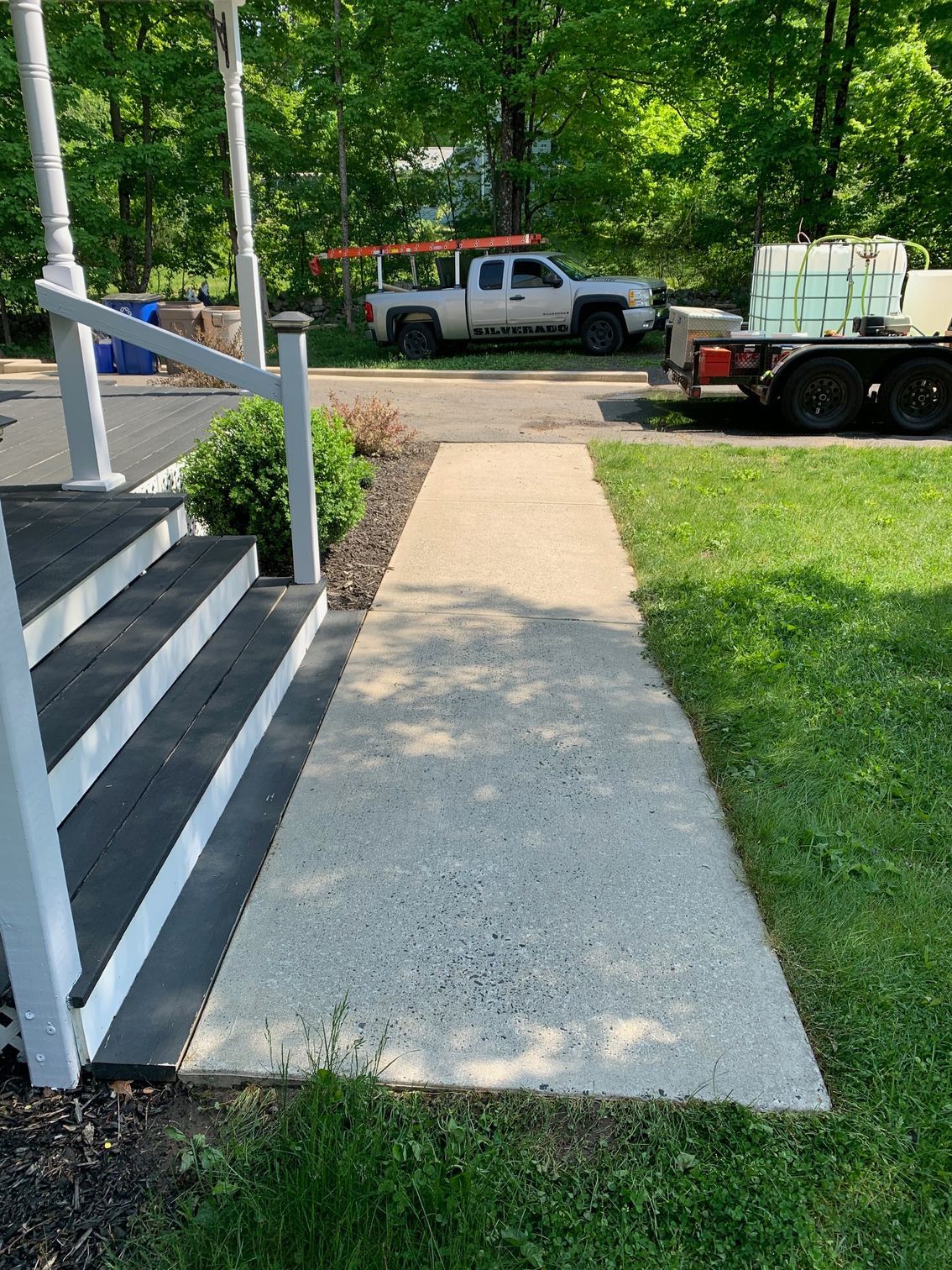 Concrete walkway leading from a porch with steps towards a road. A white truck and trailer are visible in the background.