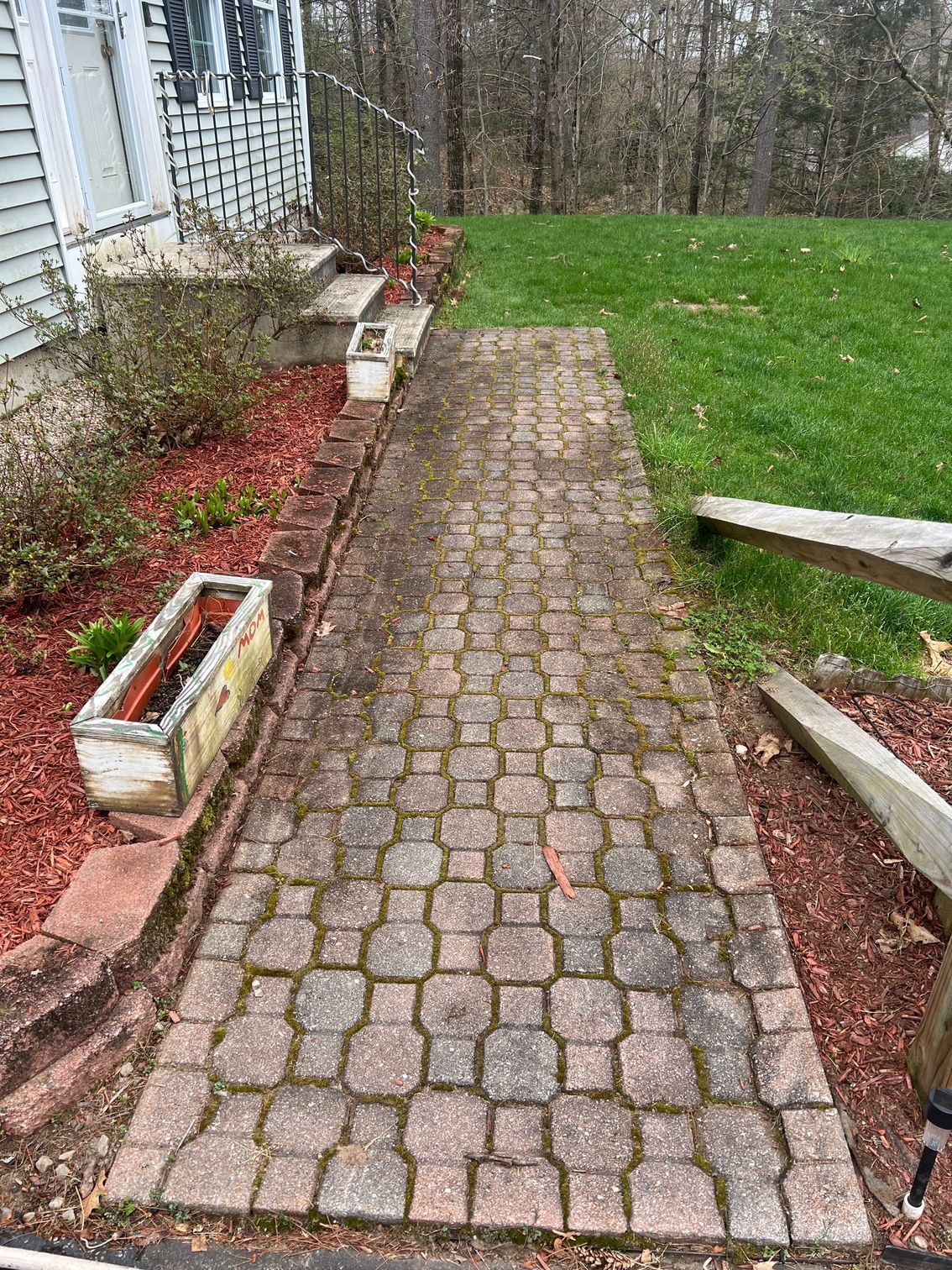Brick pathway leading to a house with a white exterior, bordered by red mulch and a planter box.
