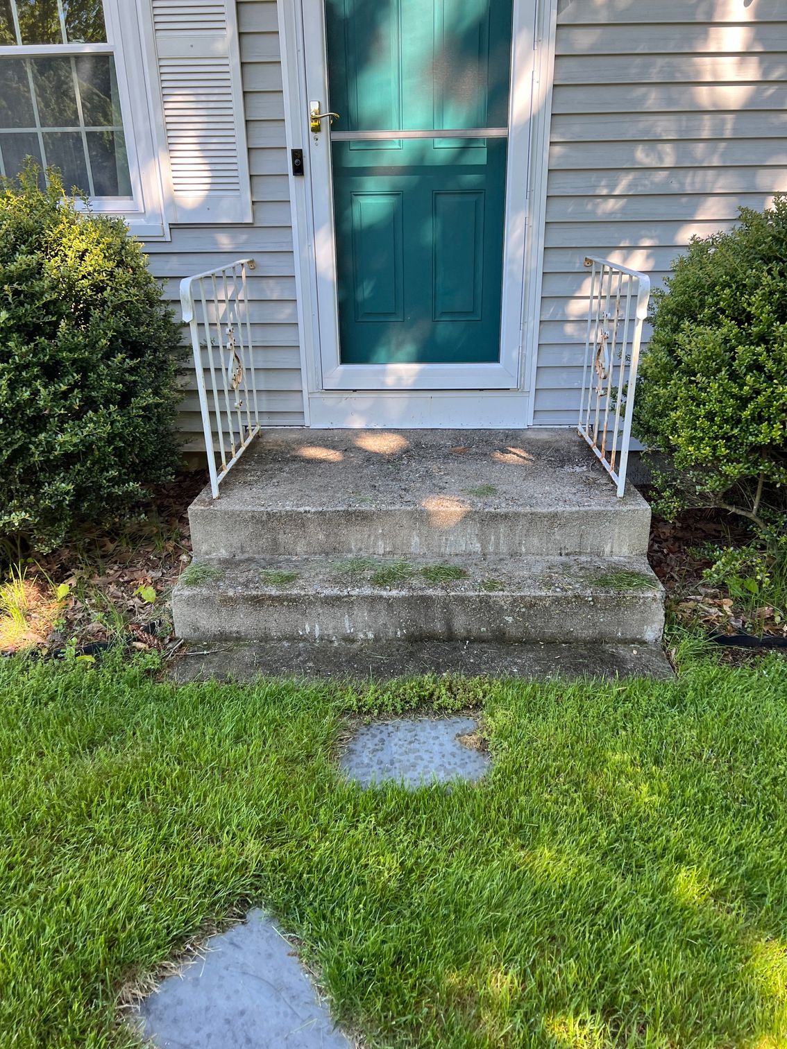 The front steps of a house with a green door and a white railing.