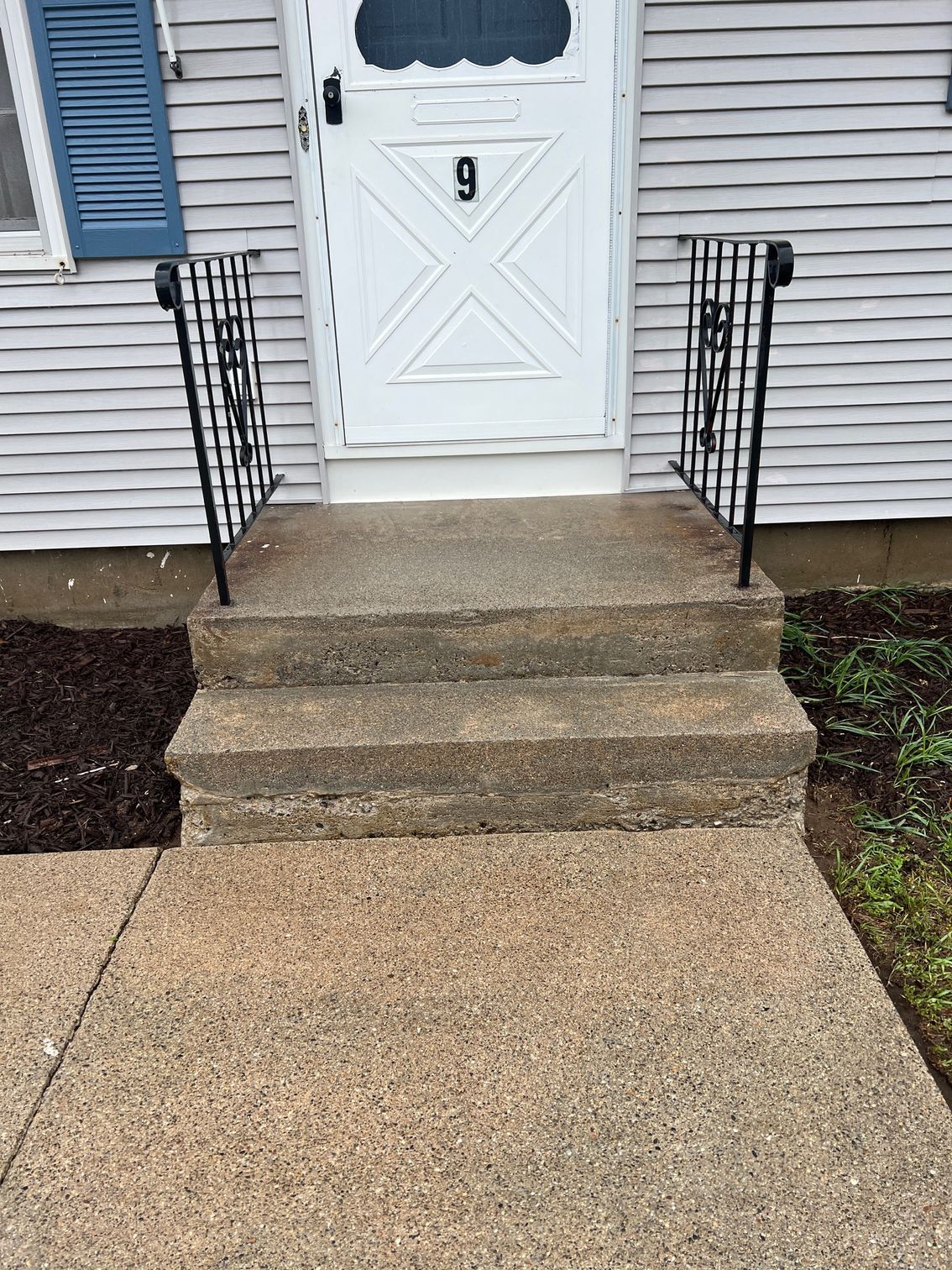 Concrete steps leading to a white door with the number 9. Black wrought-iron handrails flank the steps.