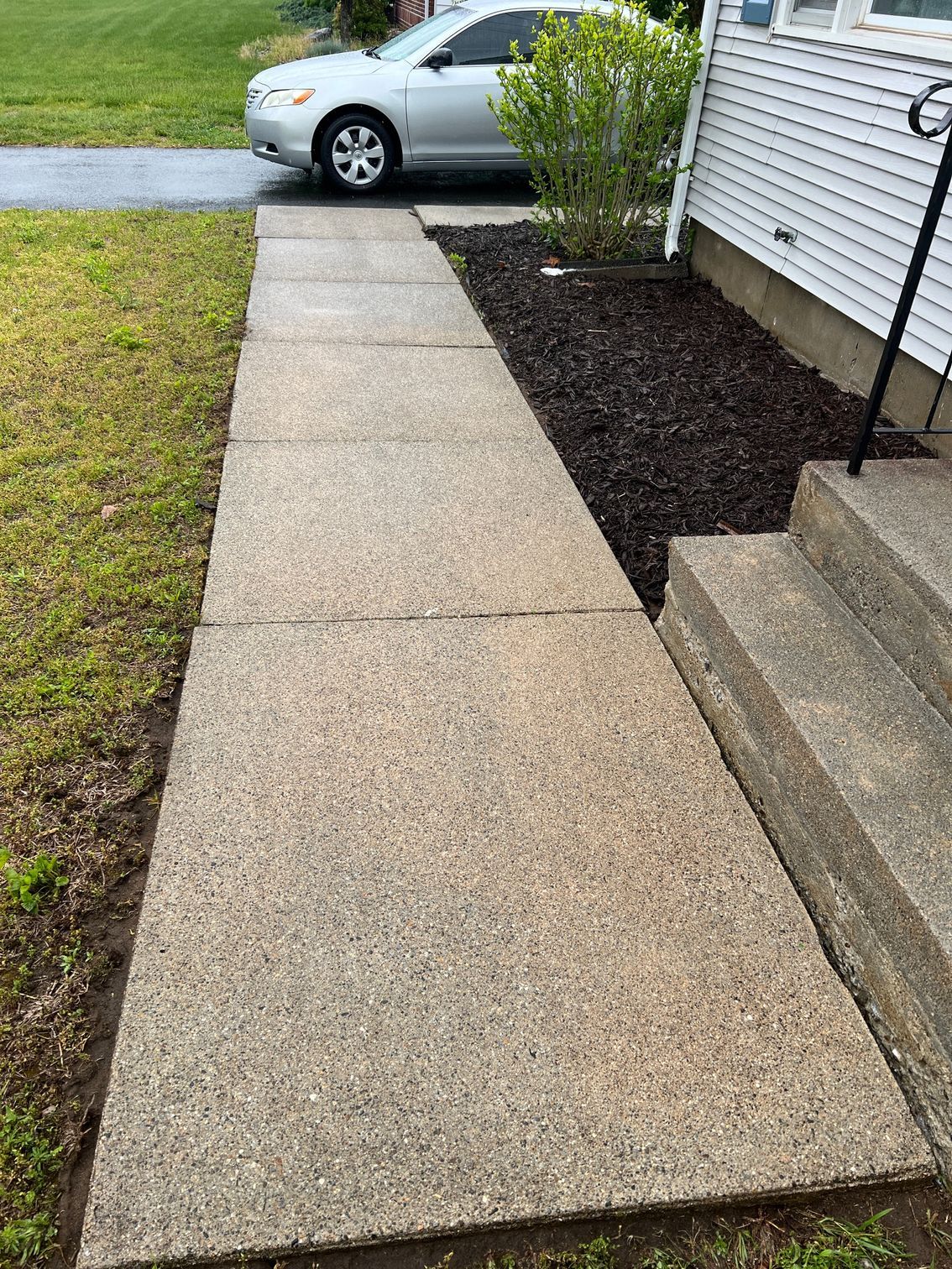 Concrete walkway leading to a house entrance with steps. A silver car is parked on the driveway.
