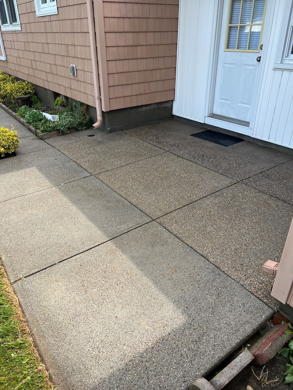 A concrete sidewalk in front of a house with a white door.