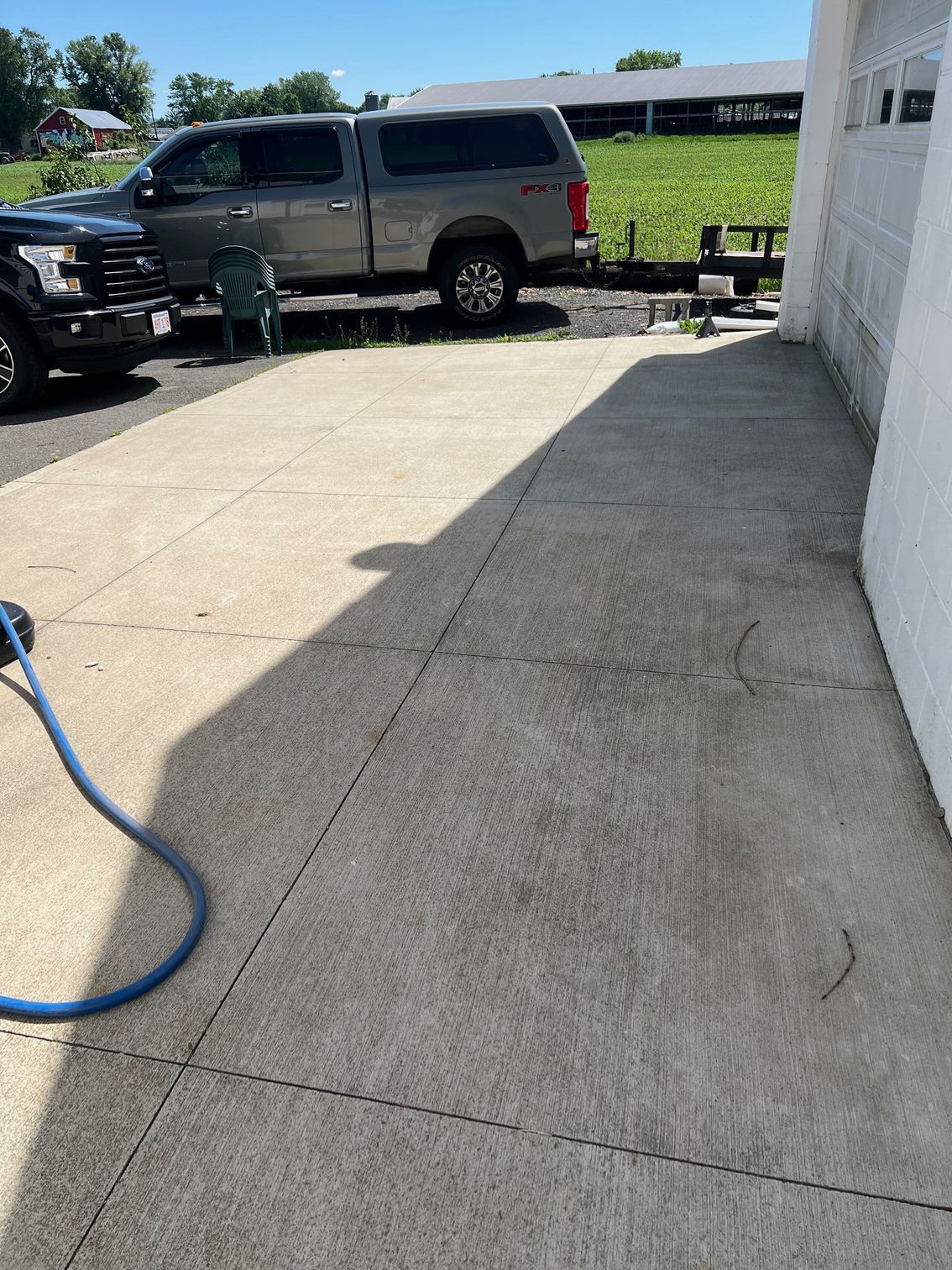 Concrete driveway next to a white building. A truck is parked on the driveway. A blue hose lies on the concrete.