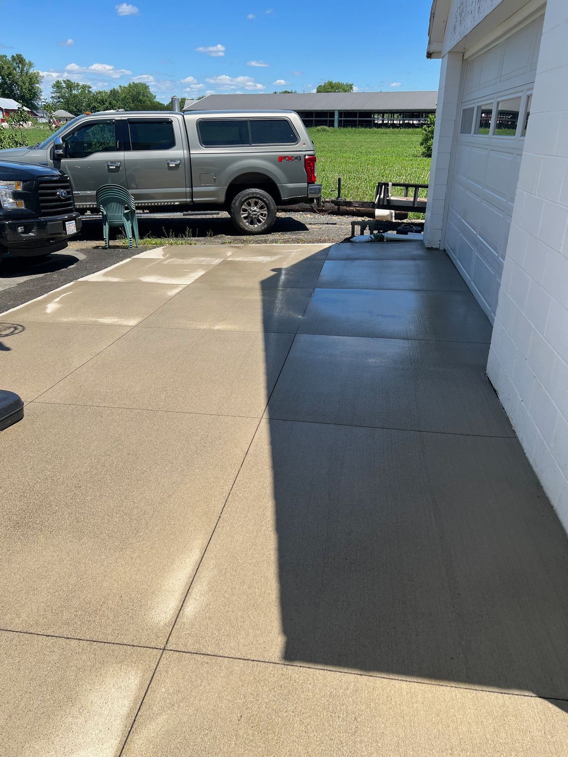 A concrete driveway next to a white building, with a truck and other objects visible.