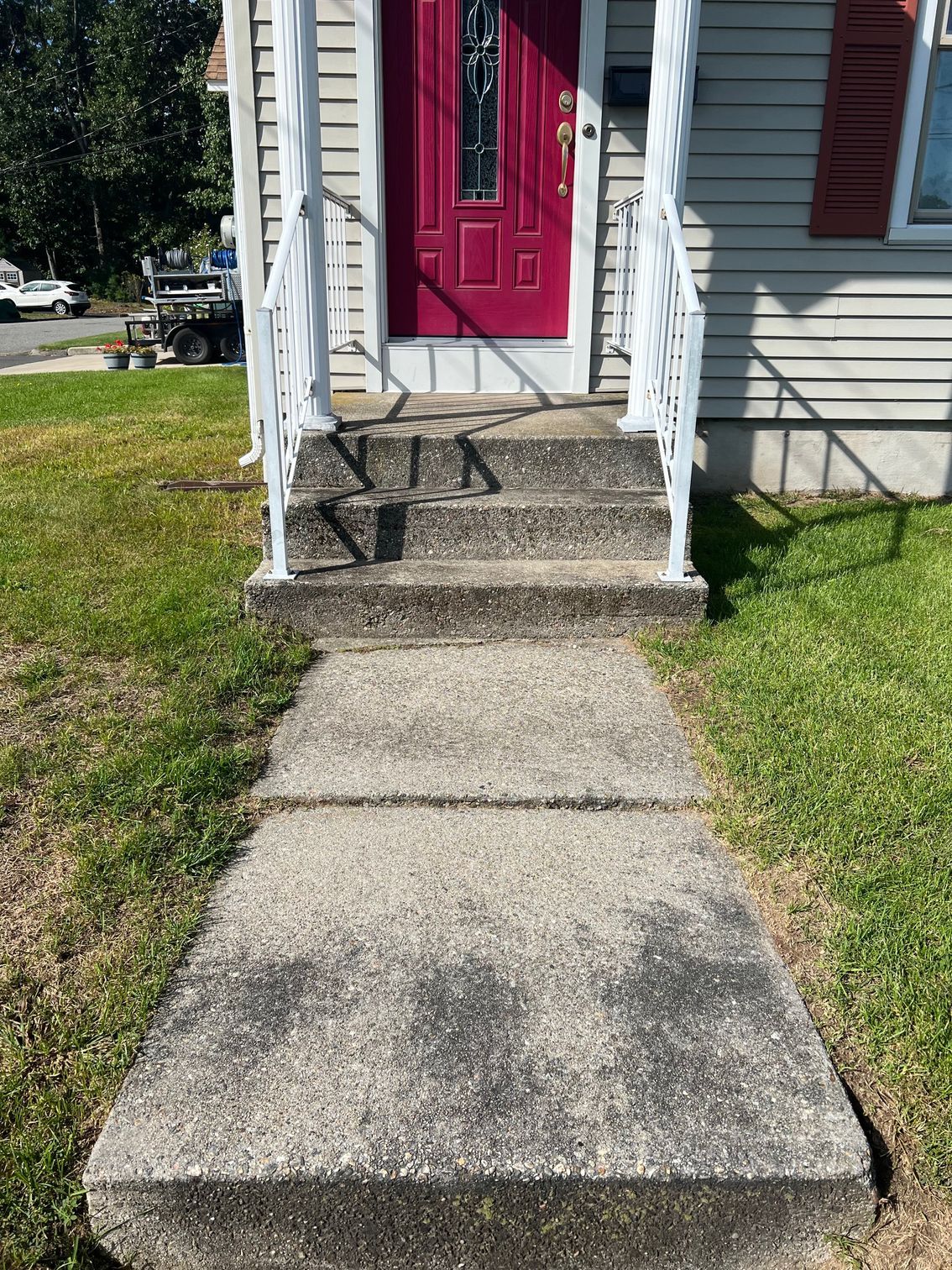Concrete path leading to a house with a red door. Steps up to the door are visible.