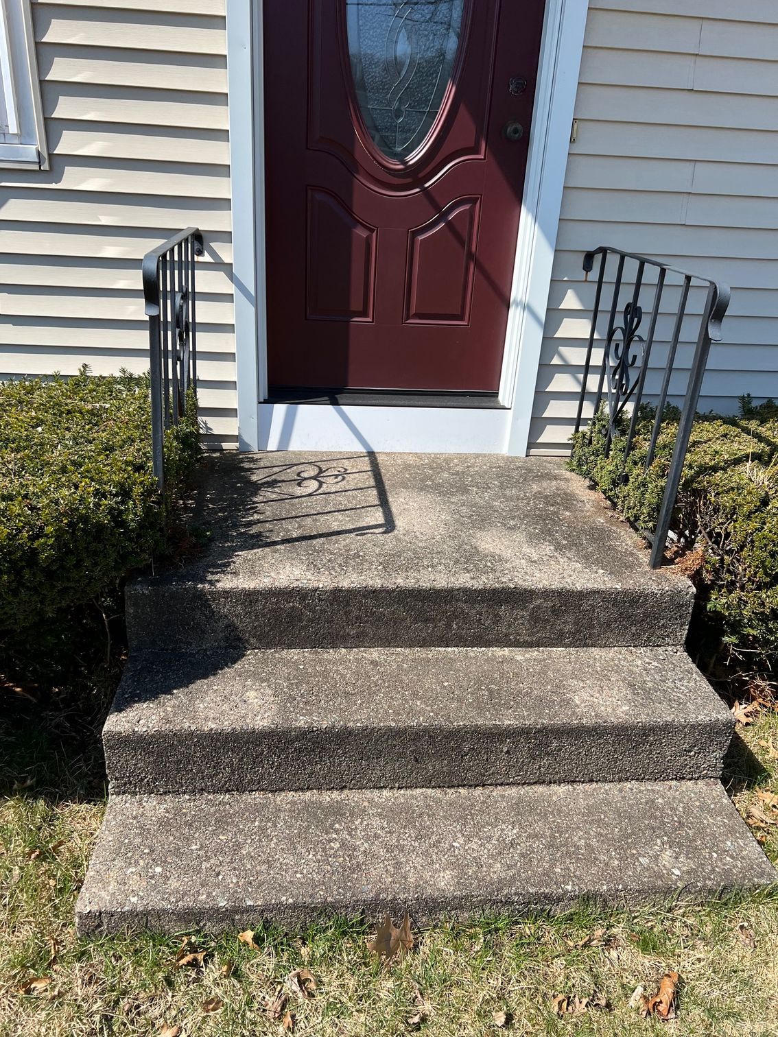 Concrete steps leading up to a burgundy door. Black railing on either side.