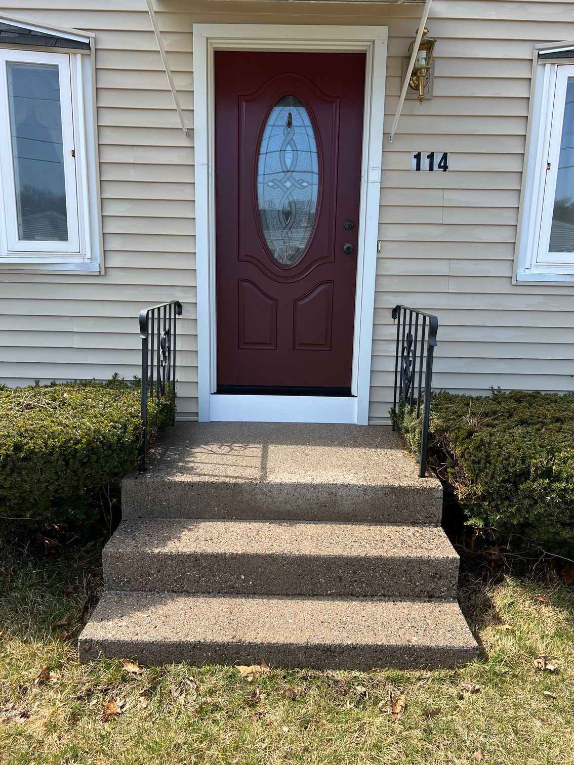 Exterior of a beige house with a red front door and three concrete steps leading up.  Handrails and windows flank the door.