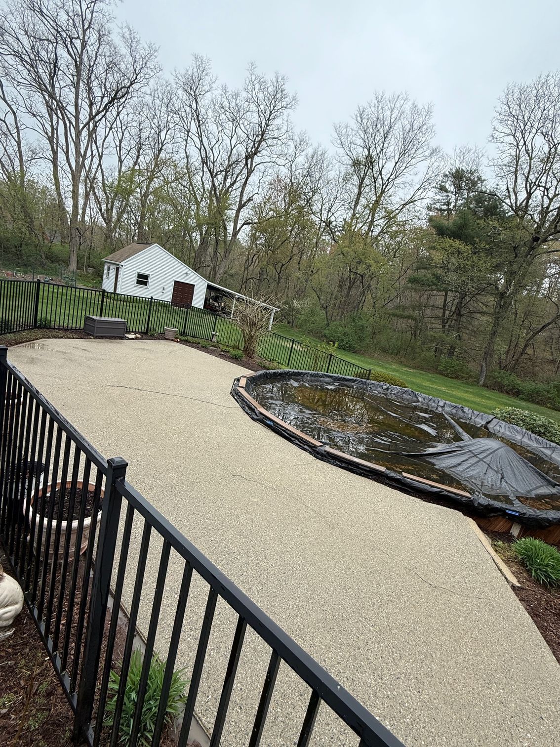 A fence surrounds a gravel driveway with a pond in the middle of it.