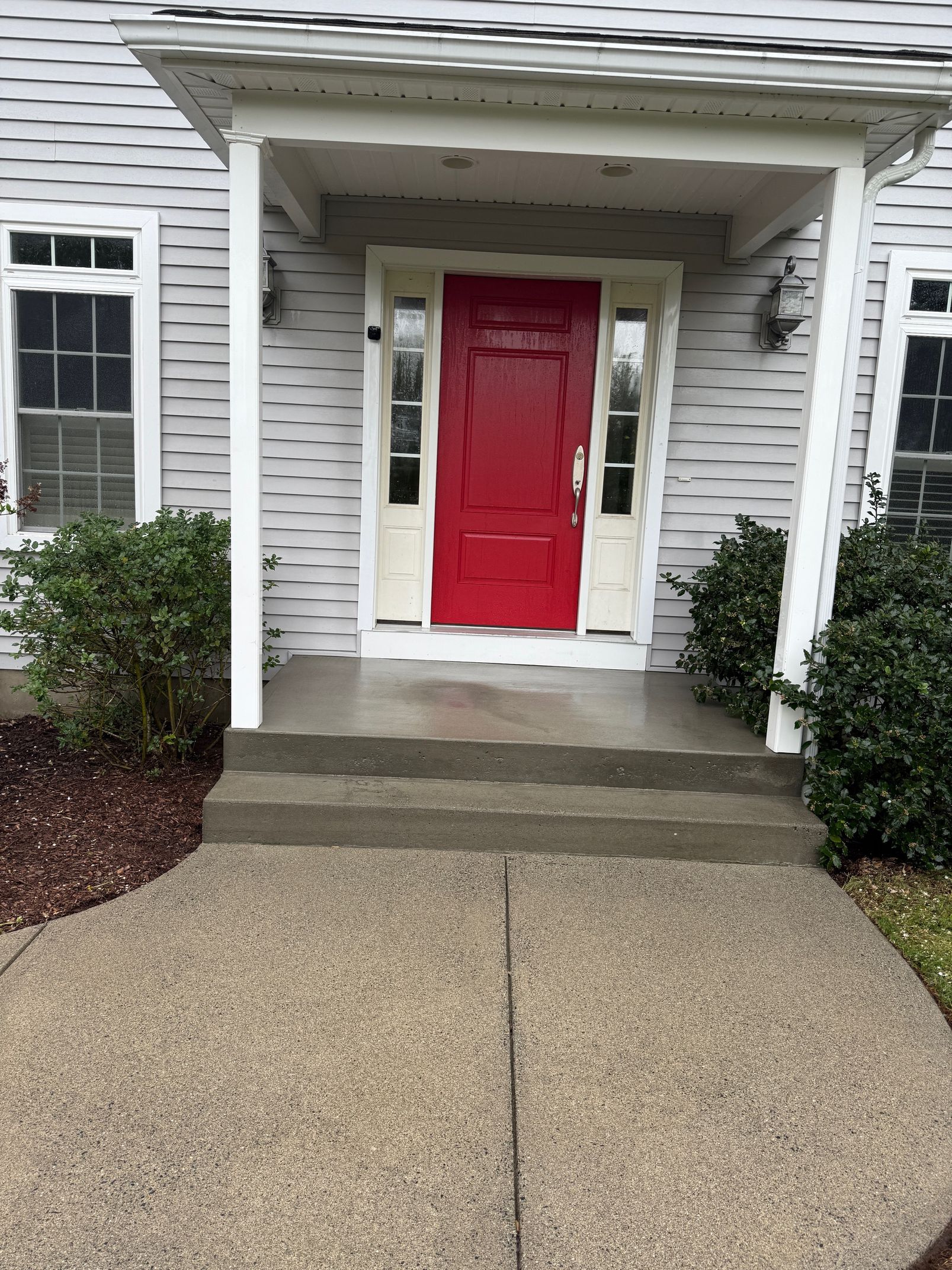 Red front door on a house with light gray siding and white trim. Two steps lead up to the covered entrance.