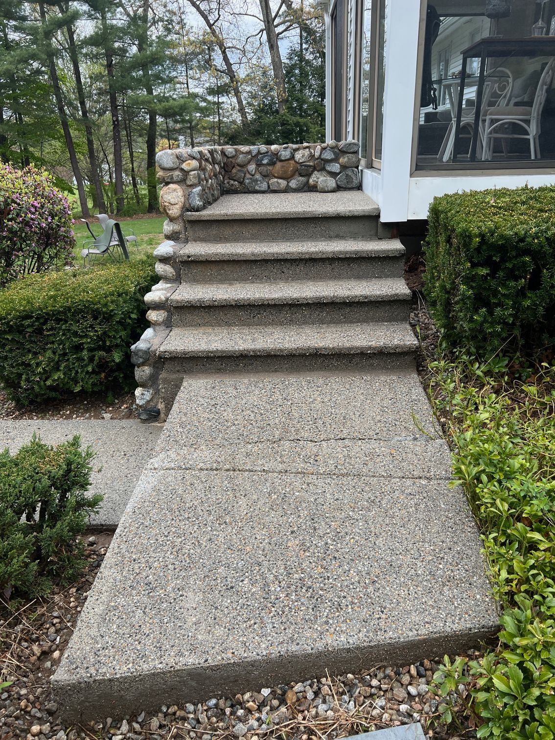 Concrete steps and walkway leading to a building with a stone accent. Green bushes flank the path.