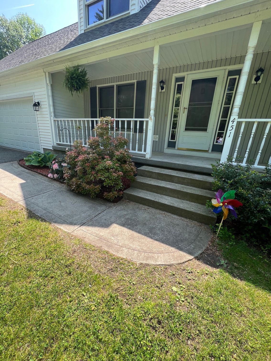 A house with a porch and steps, approached by a curved walkway. A colorful pinwheel sits in the front yard.
