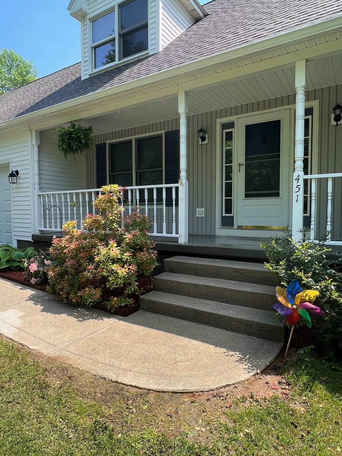 A house with a porch and stairs and a pinwheel in front of it.