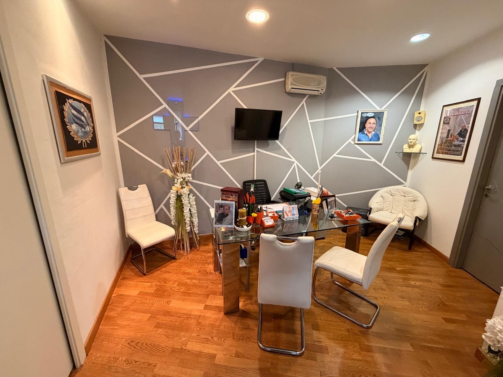 Sala da pranzo con tavolo in vetro, sedie bianche, pareti grigie con decorazioni a linee bianche e televisore a parete.