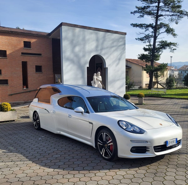 Una station wagon sportiva bianca parcheggiata sul selciato di fronte a una cappella con una statua sulla soglia.