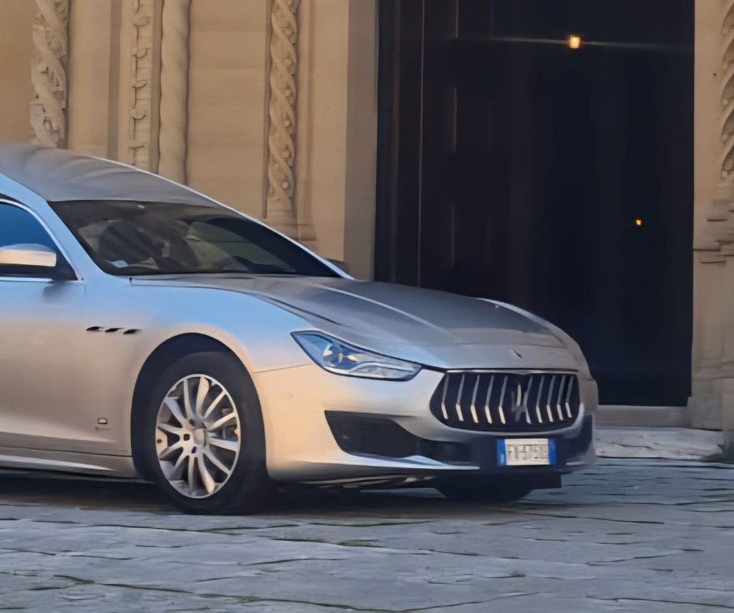 Berlina argentata parcheggiata davanti all'ingresso di un edificio con porta scura aperta.