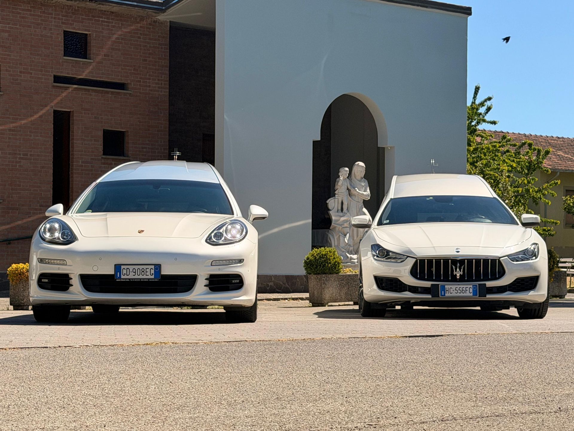 Due berline di lusso bianche parcheggiate fianco a fianco di fronte a un edificio moderno