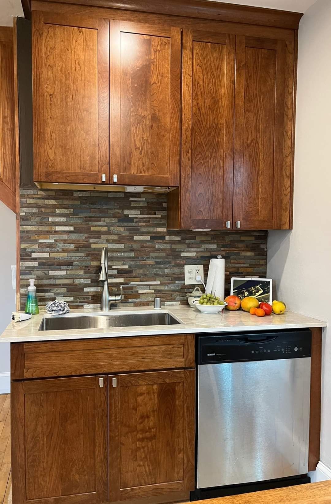 Small kitchen with wooden cabinets, stainless steel sink and dishwasher, mosaic tile backsplash.