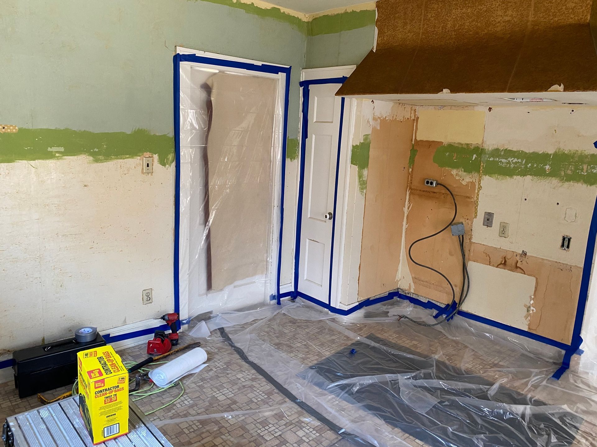 Room being renovated, with protective plastic sheeting and blue painter's tape covering doors and walls.