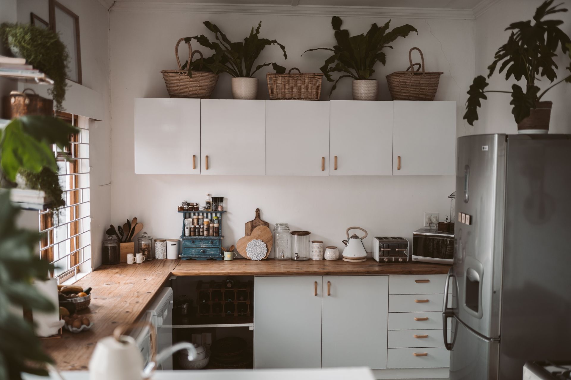 White kitchen with wooden countertops, white cabinets, and plants on top.