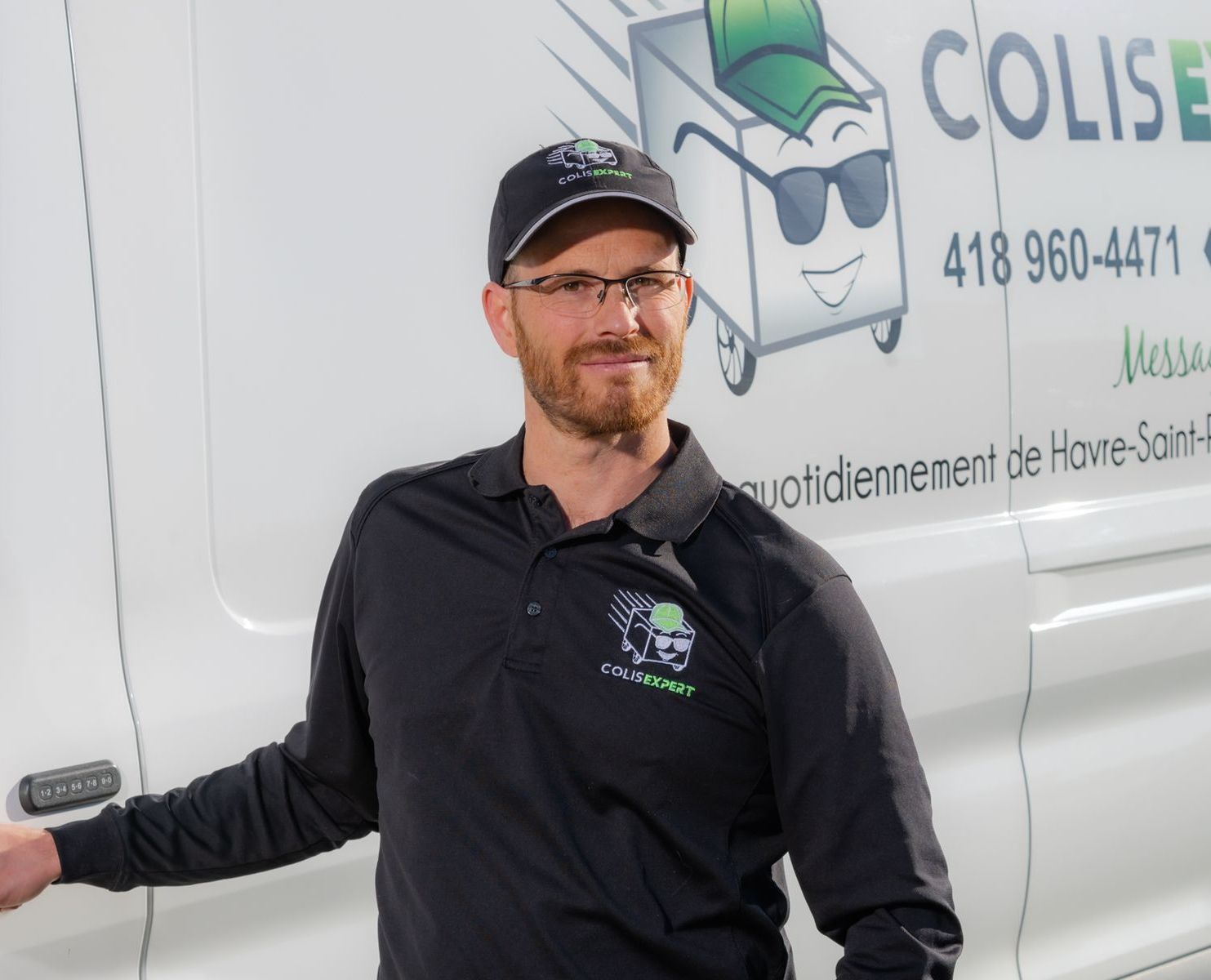 Un homme souriant, portant une casquette noire, se tient à côté d'une camionnette de livraison blanche arborant le logo et le numéro de téléphone de l'entreprise.