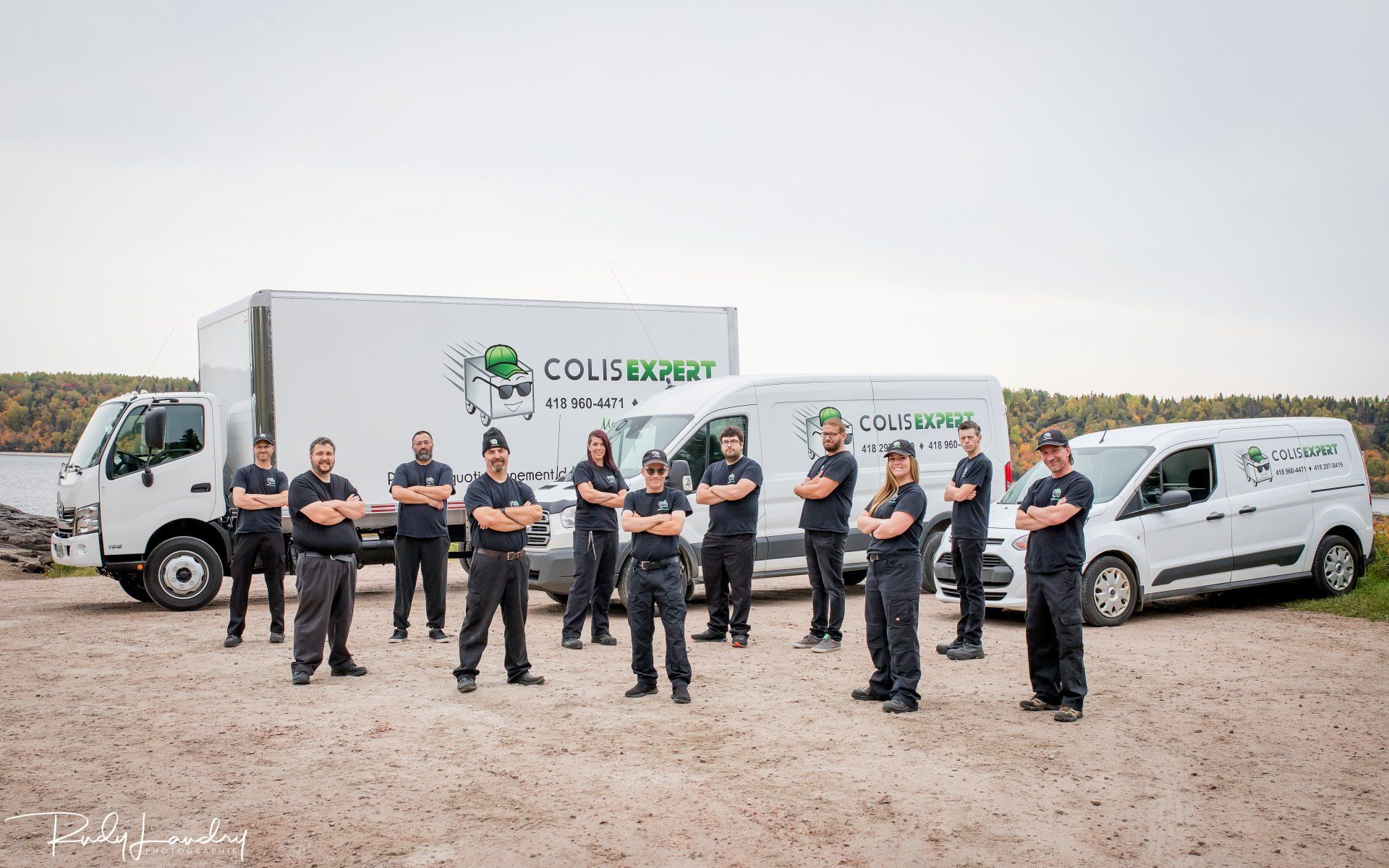 Des ouvriers se tiennent devant un camion porte-conteneurs Colls et une camionnette blanche sur un chantier de construction.