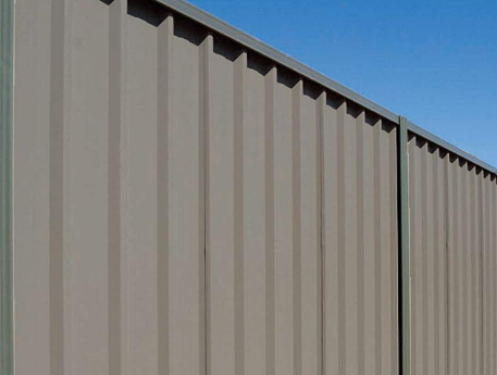 Tan corrugated metal fence against a clear blue sky.