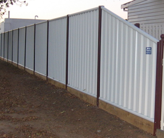White corrugated metal fence with dark brown posts, on a slightly sloped dirt ground.
